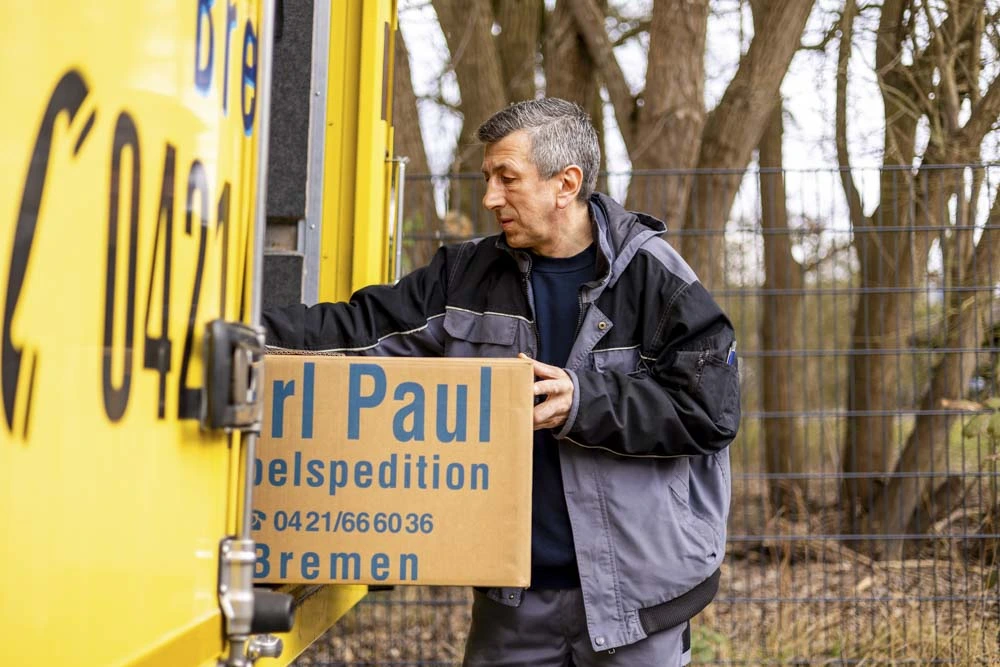 Person mit Umzugskarton vor einem Möbelwagen